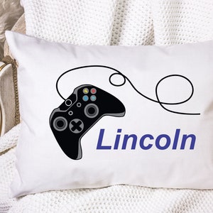 May include: White pillow with a black video game controller and the name "Lincoln" in blue text.