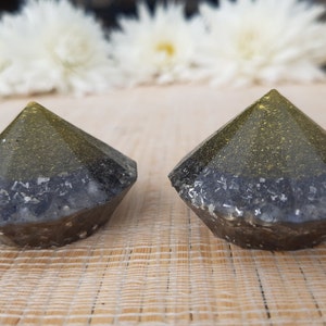 Puede incluir: Dos pisapapeles de resina en forma de diamante, negros y dorados. Los pisapapeles tienen una base negra y una parte superior dorada con purpurina.