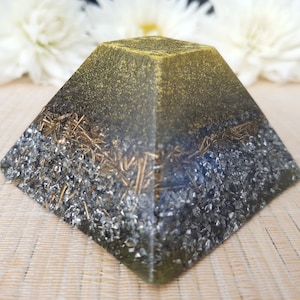 May include: A green and black crystal pyramid with gold flecks. The pyramid is made of clear resin and has a smooth, polished finish.