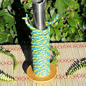 Peut inclure: Un tuyau en métal enveloppé de corde bleue et jaune avec une base dorée. Le tuyau est posé sur un tapis tissé.