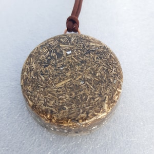 Op de afbeelding: Een ronde, bruine en gouden hanger met een bruin koordsnoer. De hanger is gemaakt van hars en heeft een getextureerd oppervlak.