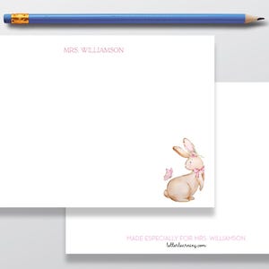 May include: White stationery with a watercolor illustration of a bunny wearing a pink bow and a butterfly. The text "MRS. WILLIAMSON" is printed in pink. A blue pencil rests at the top.