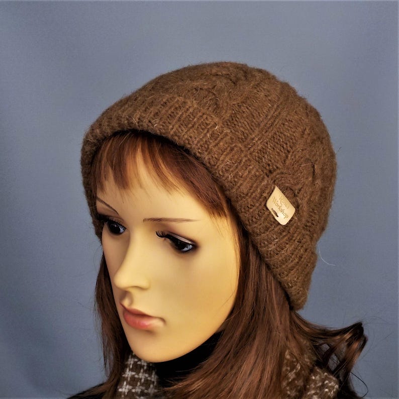 Cable design unisex beanie hat, hand-knit from rare breed Castlemilk Moorit wool at Roses Workshop. Shown with the welt turned up on a female model head. Natural undyed toffee brown pure British wool.