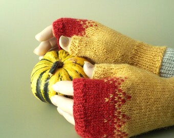 Puede incluir: Un par de guantes de punto sin dedos con un patrón de color degradado que transiciona de un rojo intenso en las puntas de los dedos a un amarillo dorado, con una pequeña calabaza rayada amarilla y verde sostenida entre las manos.