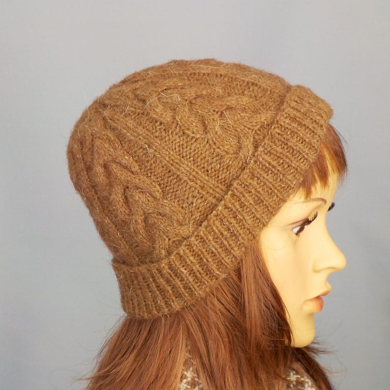 Cable design unisex beanie hat, hand-knit from rare breed Castlemilk Moorit wool at Roses Workshop. Shown with the welt turned up on a female model head. Natural undyed toffee brown pure British wool.