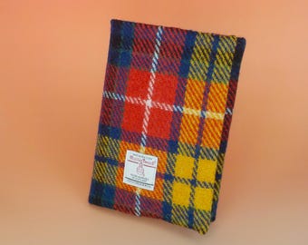Puede incluir: Una muestra de tela Harris Tweed rectangular con un vibrante patrón de cuadros en rojo, amarillo, azul y verde. Una etiqueta rectangular blanca está cosida en la esquina inferior izquierda, mostrando el texto Harris Tweed, Outer Hebrides of Scotland, 100% Pure New Wool.