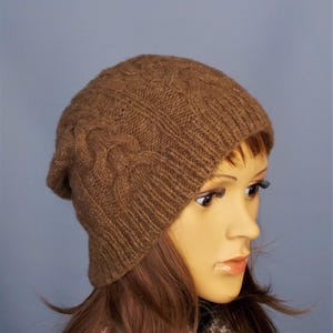 Cable design unisex beanie hat, hand-knit from rare breed Castlemilk Moorit wool at Roses Workshop. Shown with the welt turned down on a female model head. Natural undyed toffee brown pure British wool.