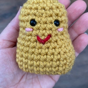 May include: A crocheted potato toy with a smiling face. The potato is yellow and has black eyes, pink cheeks, and a red smile.