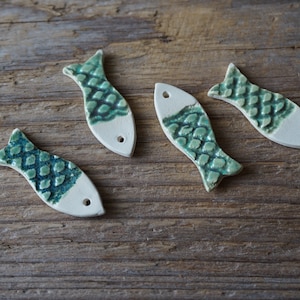 May include: Four ceramic fish ornaments with a green and white glaze. The fish have a scale pattern and are arranged on a wooden surface.