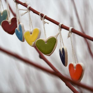 May include: A branch with seven ceramic heart ornaments hanging from it. The hearts are in various colors, including red, blue, yellow, green, and teal.
