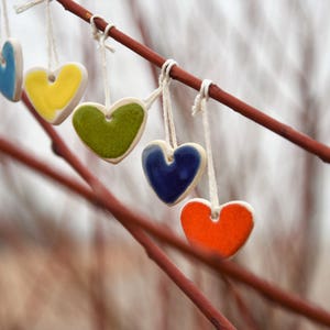 May include: A string of six ceramic hearts in various colors, including red, blue, yellow, green, and orange, hanging from a branch.