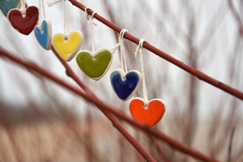 May include: A string of six ceramic hearts in various colors, including red, blue, yellow, green, and orange, hanging from a branch.
