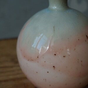 K&ouml;nnte beinhalten: Eine runde, hellrosa und blaue Keramikvase mit braunen Flecken. Die Vase hat eine breite &Ouml;ffnung und einen schmalen Hals.