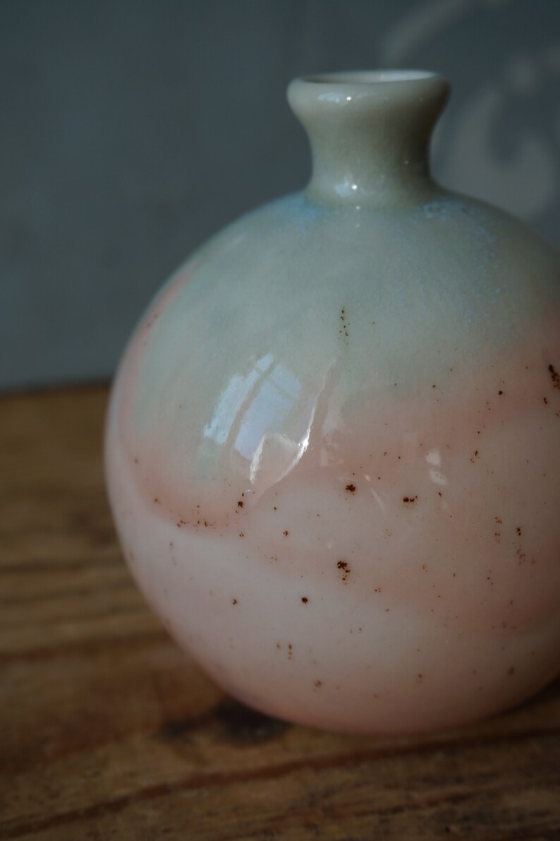 K&ouml;nnte beinhalten: Eine runde, hellrosa und blaue Keramikvase mit braunen Flecken. Die Vase hat eine breite &Ouml;ffnung und einen schmalen Hals.