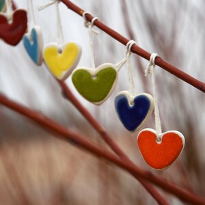 May include: A string of ceramic heart ornaments in various colors, including red, blue, green, yellow, and orange, hanging from a branch.