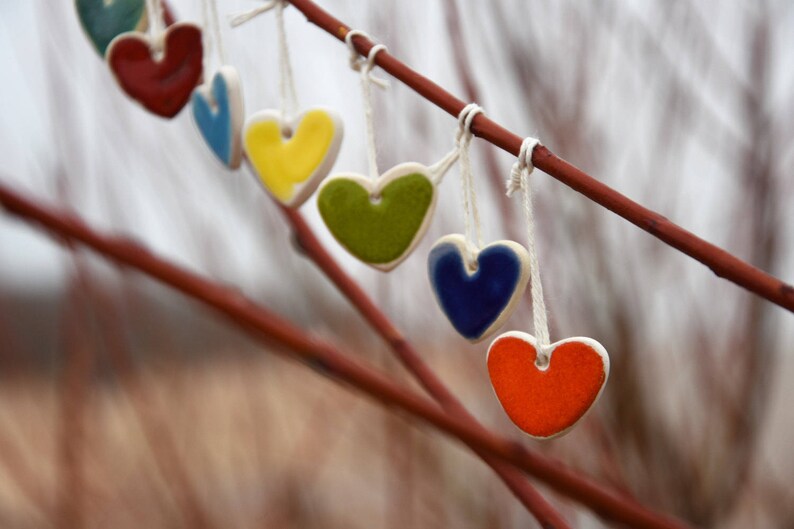 May include: A string of ceramic heart ornaments in various colors, including red, blue, green, yellow, and orange, hanging from a branch.