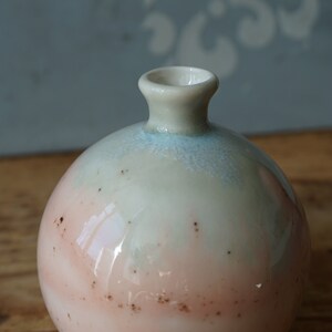 K&ouml;nnte beinhalten: Eine kleine, runde Keramikvase mit hellblauer und rosafarbener Glasur. Die Vase hat eine breite &Ouml;ffnung und einen schmalen Hals.
