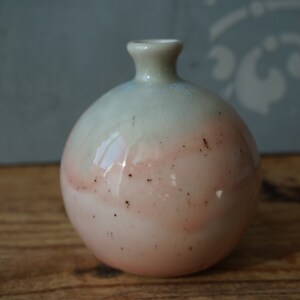 K&ouml;nnte beinhalten: Eine kleine, runde Keramikvase mit hellblauem und rosafarbenem &Uuml;berzug. Die Vase hat einen gesprenkelten braunen &Uuml;berzug und eine leicht ausgestellte &Ouml;ffnung.