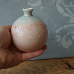 K&ouml;nnte beinhalten: Eine kleine, runde Keramikvase mit hellblauer und rosafarbener Glasur. Die Vase hat eine gesprenkelte Oberfl&auml;che und eine schmale &Ouml;ffnung oben.