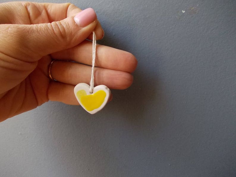 May include: A white ceramic heart pendant with a yellow painted design, hanging from a white string.