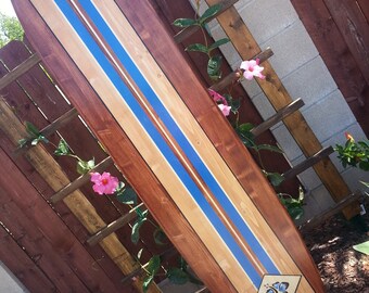 May include: A wooden surfboard with blue and white stripes and a butterfly design. The surfboard is leaning against a wooden fence.