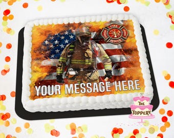 May include: Rectangular cake with white frosting and a decorative image of a firefighter in front of an American flag. The cake has the text "YOUR MESSAGE HERE" and a fire department emblem. The cake is on a black tray.