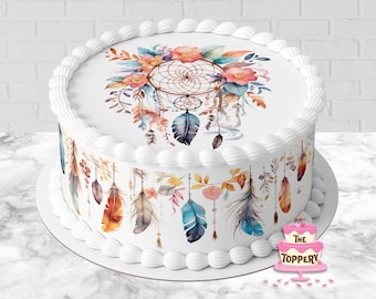 May include: A white cake decorated with a watercolour dreamcatcher design. The dreamcatcher is surrounded by feathers and flowers in shades of blue, orange, and pink. The cake is also decorated with a white frosting border and a pink and white cake topper that says "The Toppery".
