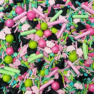 May include: A colorful mix of edible sprinkles featuring black witch hat shapes, light pink crowns, bright pink and lime green spheres, light green rods, and small pink hearts. The assortment includes various textures and sizes of sugar decorations.