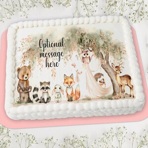 May include: A rectangular cake with white frosting and a pink base. The cake is decorated with a woodland scene featuring a bear, raccoon, bunny, fox, owl, hedgehog, and deer. The text "Optional message here" is above the animals.