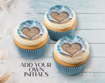 May include: Three cupcakes with blue liners and white frosting. Each cupcake has a beach-themed edible image with a heart and the initials "D+L". The text "ADD YOUR OWN INITIALS" is also visible.