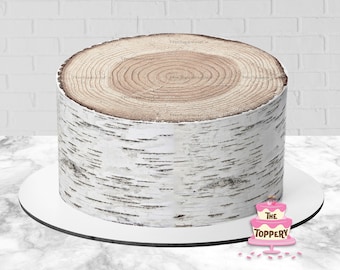 May include: A round cake with a birch tree trunk design. The cake has a light brown top with concentric circles and a white and black birch bark pattern on the sides. It sits on a white cake board.