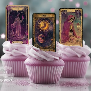 May include: Three cupcakes decorated with tarot card toppers. The cards are The Magician, The Sun, and Death. The cupcakes are frosted with purple frosting and topped with white frosting.
