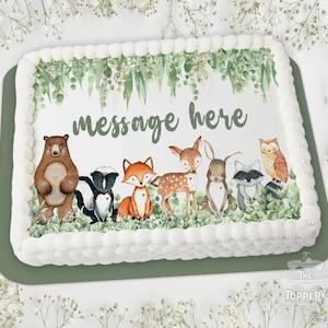 May include: A white cake with green leaves and woodland animals, including a bear, fox, deer, rabbit, skunk, and owl. The cake is decorated with the text "message here".