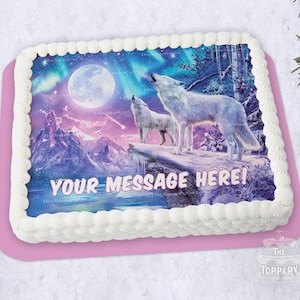May include: A rectangular cake with a winter wolf scene. Two white wolves howl at the moon under a colorful aurora borealis. The cake has white frosting with a pink base and the text "YOUR MESSAGE HERE!"