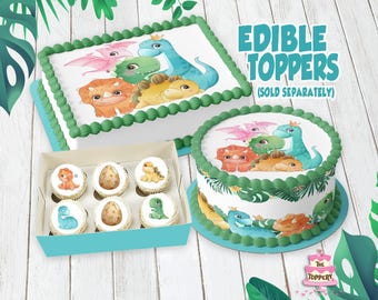 May include: A rectangular cake and a round cake, both decorated with green frosting borders and edible dinosaur illustrations, alongside a light blue box containing six cupcakes featuring individual dinosaur and egg images. Text reads EDIBLE TOPPERS.
