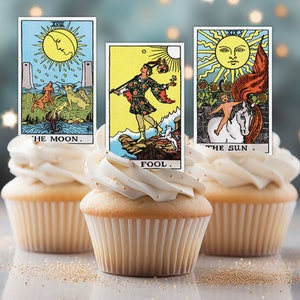 May include: Three cupcakes decorated with tarot card toppers. The cards are The Moon, The Fool, and The Sun.