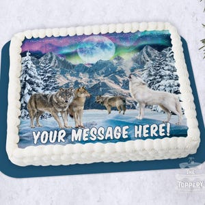 May include: A rectangular cake with white frosting and a blue base. The cake features a winter scene with wolves, mountains, and a full moon under the aurora borealis. The text "YOUR MESSAGE HERE!" is displayed on the cake.