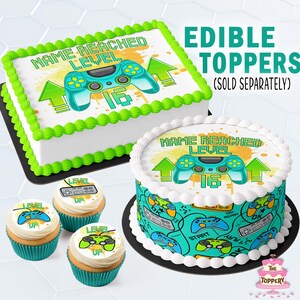 May include: A rectangular cake with green frosting borders and a round cake with white frosting borders, both featuring a teal video game controller graphic and the text NAME REACHED LEVEL 16. Three cupcakes feature similar gaming graphics.