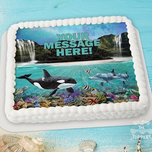 May include: A rectangular cake with white frosting and a colorful edible image. The image features an underwater scene with an orca, dolphins, and tropical fish. The text "YOUR MESSAGE HERE!" is displayed above the water line.