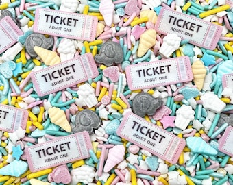 May include: A colorful assortment of edible sprinkles featuring rectangular pink tickets with the text TICKET ADMIT ONE, grey elephant shapes, pale yellow ice cream cones, white popcorn clusters, and small blue, pink, and yellow sugar rods.