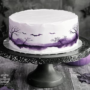 May include: A round cake with smooth white frosting featuring a dark purple watercolor-style landscape of bare trees and flying bats around the base. The cake sits on a black metal pedestal stand with a decorative filigree edge.