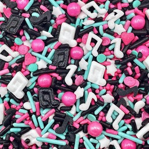 May include: A colorful mix of edible sprinkles featuring black, white, and pink musical note shapes, small white stars, tiny pink hearts, and a variety of rod-shaped sprinkles in shades of black, pink, and bright turquoise blue.