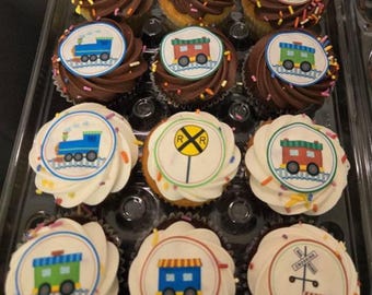 May include: A dozen cupcakes in a clear plastic container. The cupcakes have either chocolate or vanilla frosting, and are decorated with colorful train-themed edible images. Some cupcakes feature a blue train, others a red train car, and others a railroad crossing sign.