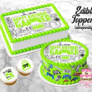May include: Two cakes and two cupcakes with a gaming theme. The rectangular cake has a green border and the text "Happy Birthday Gamer". The round cake has a green border and gaming controller graphics. The cupcakes have gaming-themed text.