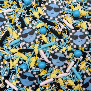 May include: A mix of colorful sprinkles with blue and white checkered squares featuring a blue face with sunglasses. The sprinkles include black, white, yellow, and blue colors.