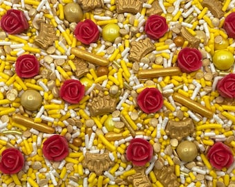 May include: A decorative sprinkle mix featuring red rose-shaped sugar pieces, metallic gold crown-shaped sugar pieces, gold spherical sugar pearls, and a combination of yellow and white rod-shaped sprinkles scattered across the entire surface.