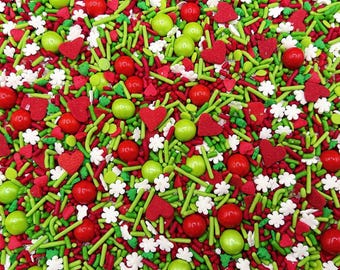 May include: A festive mix of edible sprinkles featuring red and lime green rod-shaped jimmies, small white flower-shaped sugar pieces, red heart-shaped confetti, and glossy red and lime green round candy balls scattered across the entire surface.