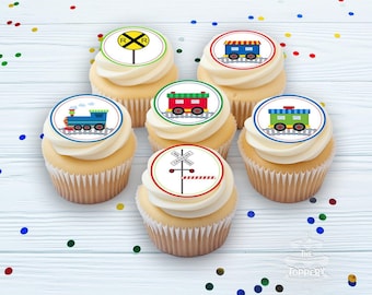 May include: Six cupcakes with white frosting and train-themed edible toppers. The toppers feature images of trains, railroad crossing signs, and a yellow railroad crossing sign. The cupcakes are on a light wood-grain surface with colorful confetti.