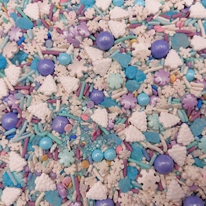 May include: A mix of blue, white, and purple sprinkles, including snowflake, tree, and star shapes, as well as small round candies.