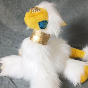 May include: White plush toy with yellow accents. The toy has a long, fluffy tail and large, yellow paws. The toy's head is yellow with a gold collar and a blue eye.